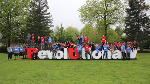 Large group of students and faculty standing on and around a 3D Rutgers Revolutionary sign.