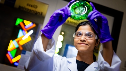 Female student looking at poured green glass in glass laboratory.