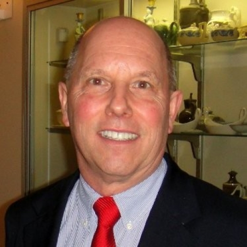 Headshot of bald male wearing a black suit jacket, light blue shirt, and a red tie.