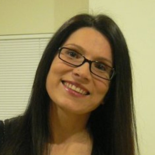Head shot of smiling female tilting her head to the side with long black hair wearing eyeglasses.