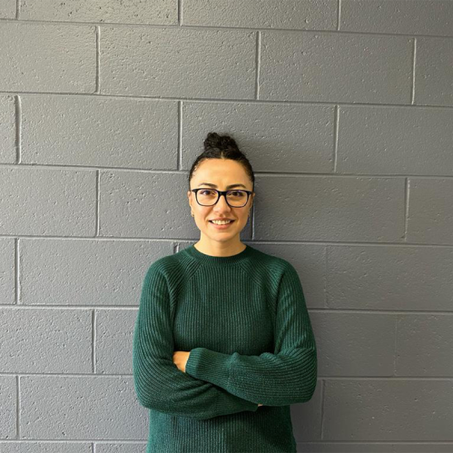 Head shot of woman with her hair up in a bun, folding her arms wearing a green sweater, eyeglasses