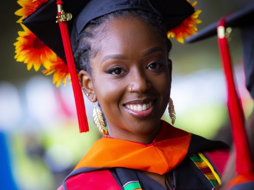 Black women during convocation ceremonies wearing black regalia with flowers on mortarboard.