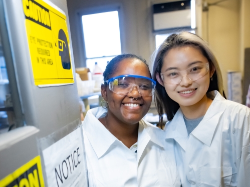 Black female doctoral student and Asian female undergraduate in white lab coats posing for a picture - Jersey Pictures