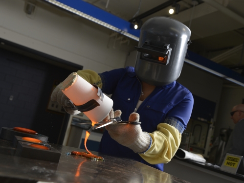 Student pouring molten glass into a mold while wearing safety equipment.