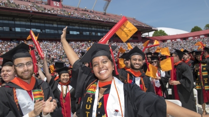 Group of male and female students in regalia celebrating their graduation in the stadium.