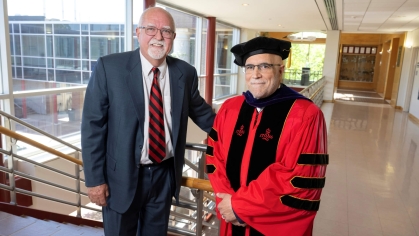 Man on left wearing a blue suit with a black and red stripped tie and man on right wearing red and black Rutgers regalia.