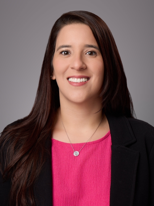 Headshot of female with long black hair wearing a necklace with a bright pink blouse under a black jacket.