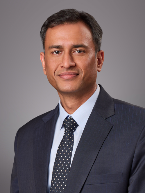 Headshot of male with short black hair wearing a black suit, tie, and w white button down shirt.