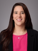 Headshot of female with long black hair wearing a necklace with a bright pink blouse under a black jacket.