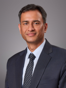Headshot of male with short black hair wearing a black suit, tie, and w white button down shirt.
