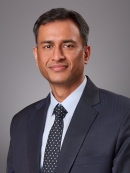 Headshot of male with short black hair wearing a black suit, tie, and w white button down shirt.