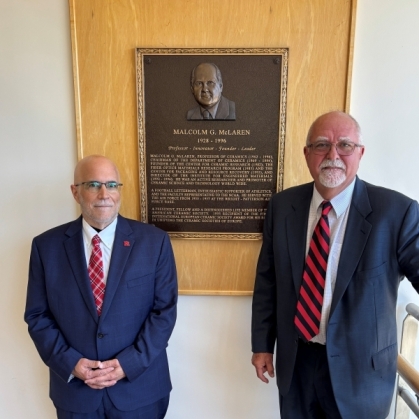 Two men dressed in suit and ties flank a wall bronze plaque at the School of Engineering.